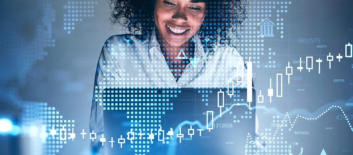 Happy young African American businesswoman using laptop at blurry table with double exposure of financial graph and digital world map. Concept of investment and trading. Toned image