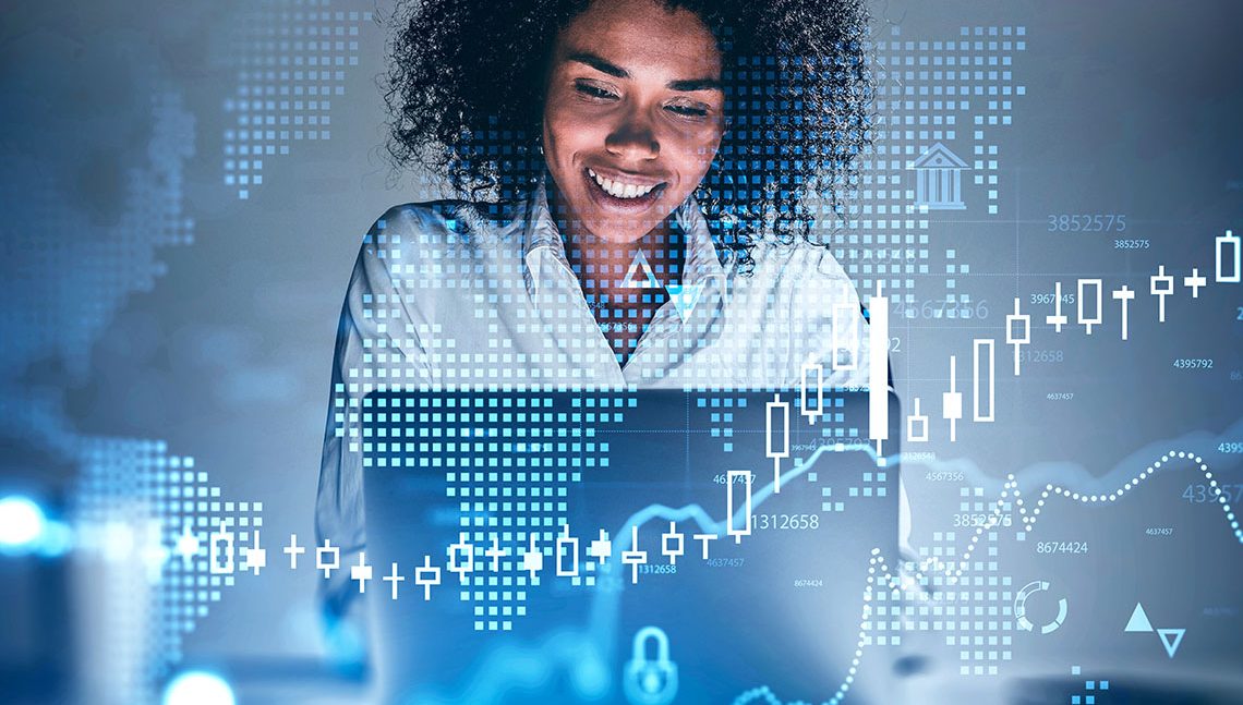 Happy young African American businesswoman using laptop at blurry table with double exposure of financial graph and digital world map. Concept of investment and trading. Toned image